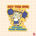 A die-cut sticker featuring a cute cartoon rabbit lifting a barbell, with the text 'HIT THE GYM' at the top and 'OUTLIFT YOUR ENEMIES' at the bottom, shown on a light pink grid background.