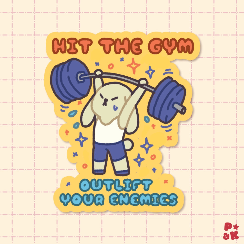 A die-cut sticker featuring a cute cartoon rabbit lifting a barbell, with the text 'HIT THE GYM' at the top and 'OUTLIFT YOUR ENEMIES' at the bottom, shown on a light pink grid background.