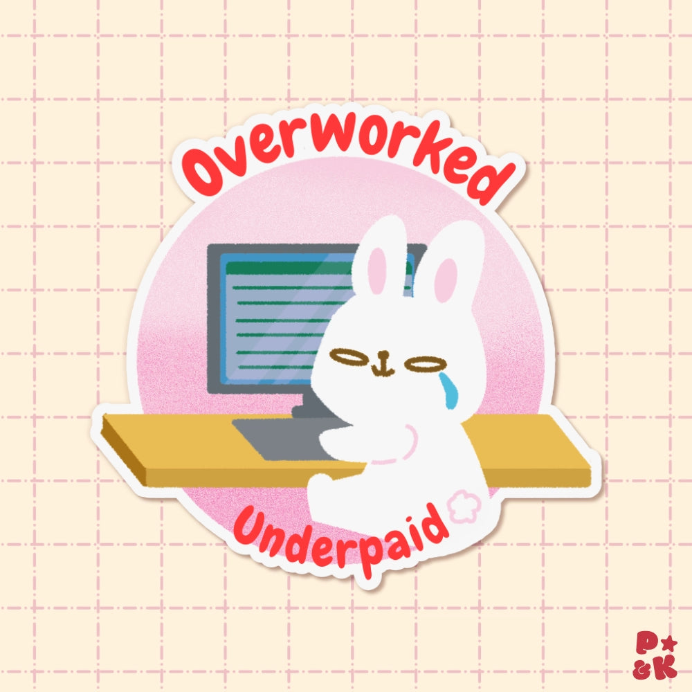 A die-cut sticker featuring a white cartoon rabbit sitting at a desk in front of a computer screen, with the words 'Overworked' above and 'Underpaid' below in red curved text, shown on a pale pink grid background.