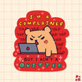 A die-cut sticker featuring a cute cartoon bear angrily looking at a laptop with the text 'I'M A COMPLAINER BUT I AIN'T A QUITTER' on a pink grid background.